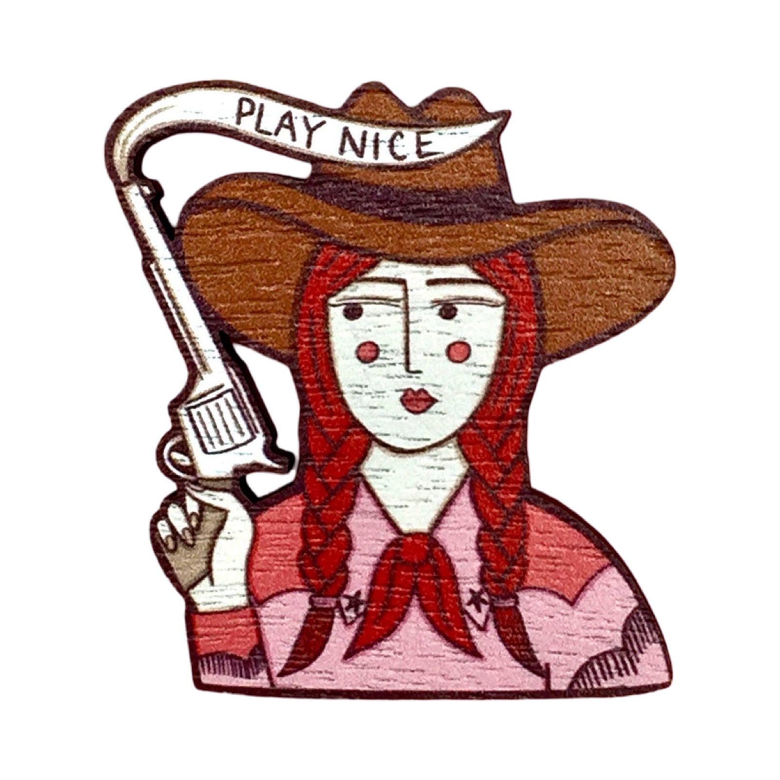 A wooden brooch featuring a cowgirl wearing a pink shirt with a white horse design, a red neckerchief and a brown cowboy hat holding a toy gun with a banner saying 'play nice'.