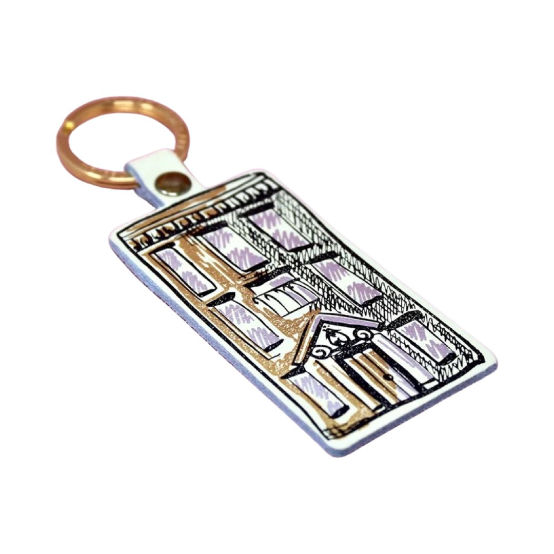 A cream rectangular leather keyring with an illustration of an apartment block in black and a gold-coloured keyring. 