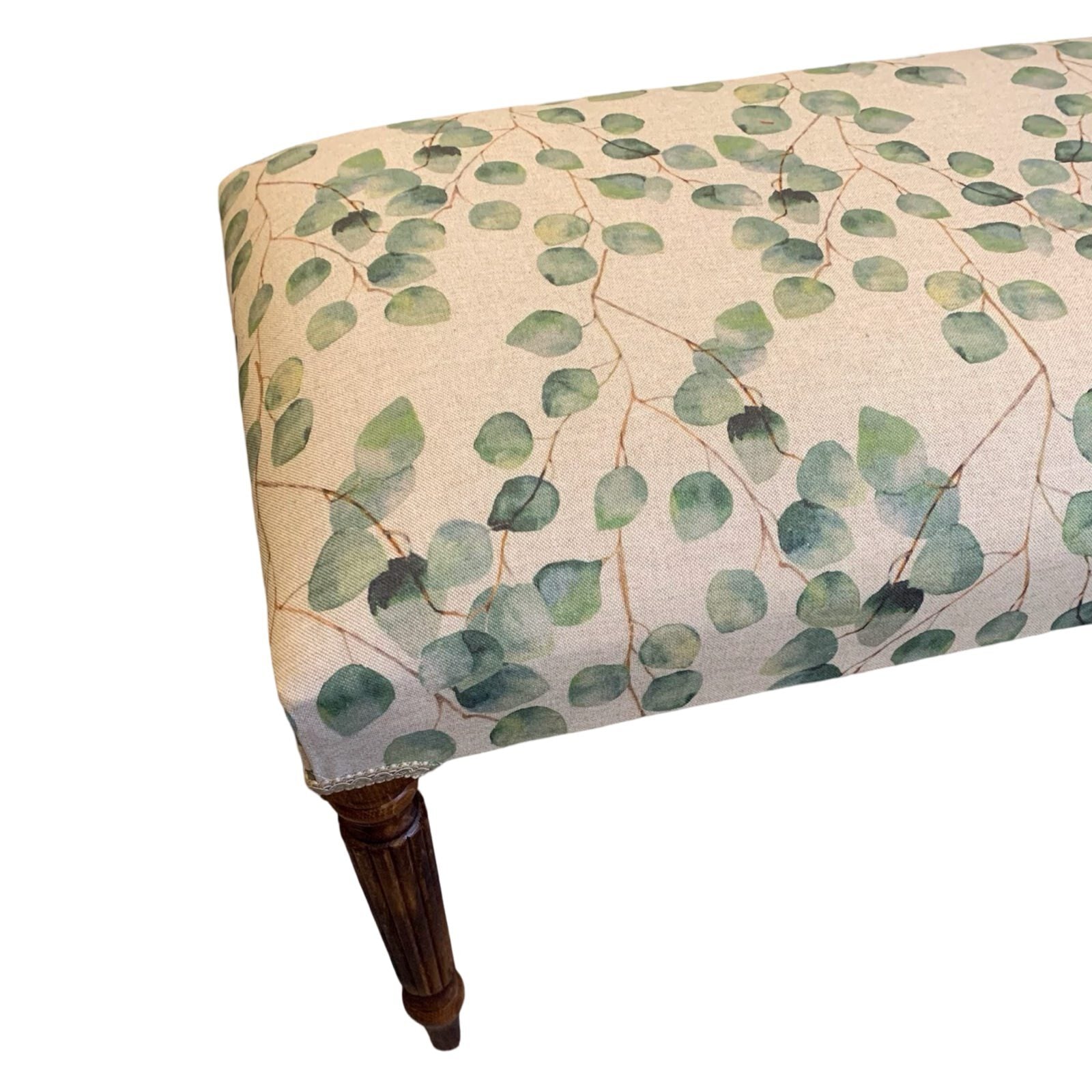 A rectangular bench with mahogany legs and cream linen fabric upholstered in a leaf pattern.