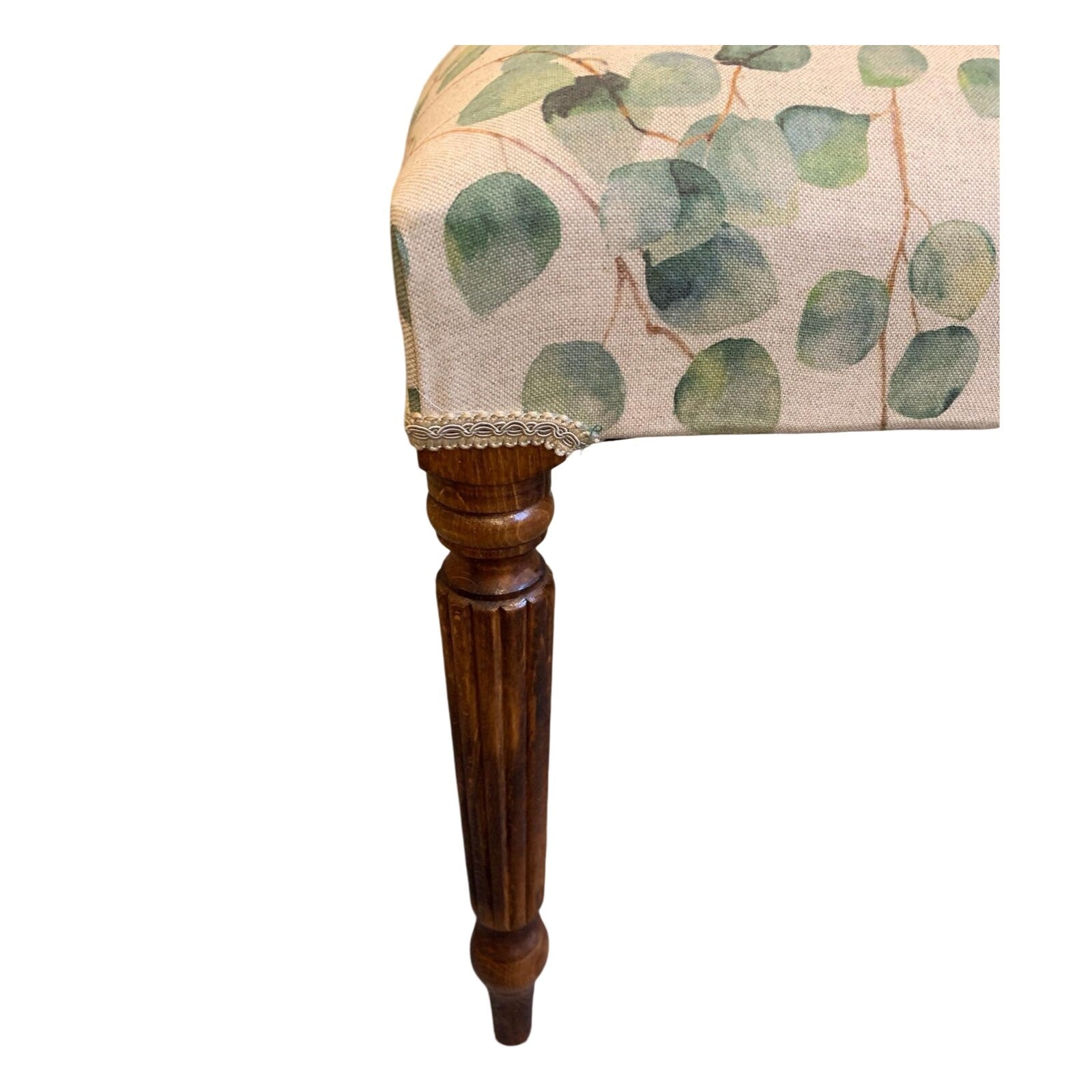 A rectangular bench with mahogany legs and cream linen fabric upholstered in a leaf pattern.