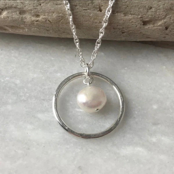 Silver necklace with a circular pendant and pearl on a stone surface.