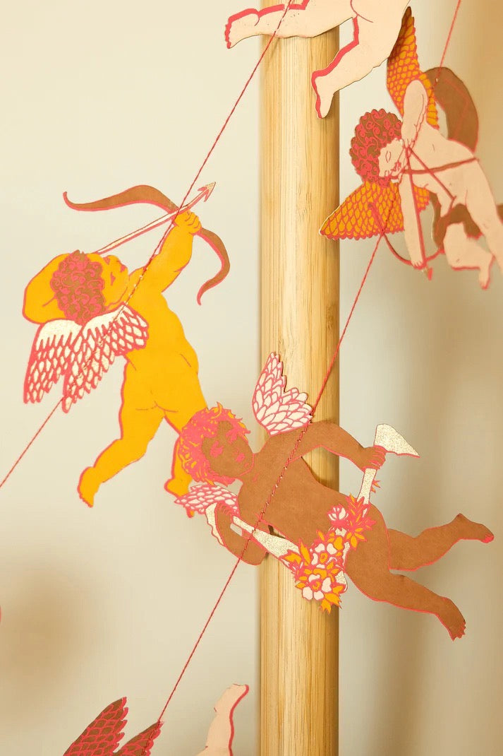 Decorative paper cutout of cherubs with a bow and arrow on a beige background.