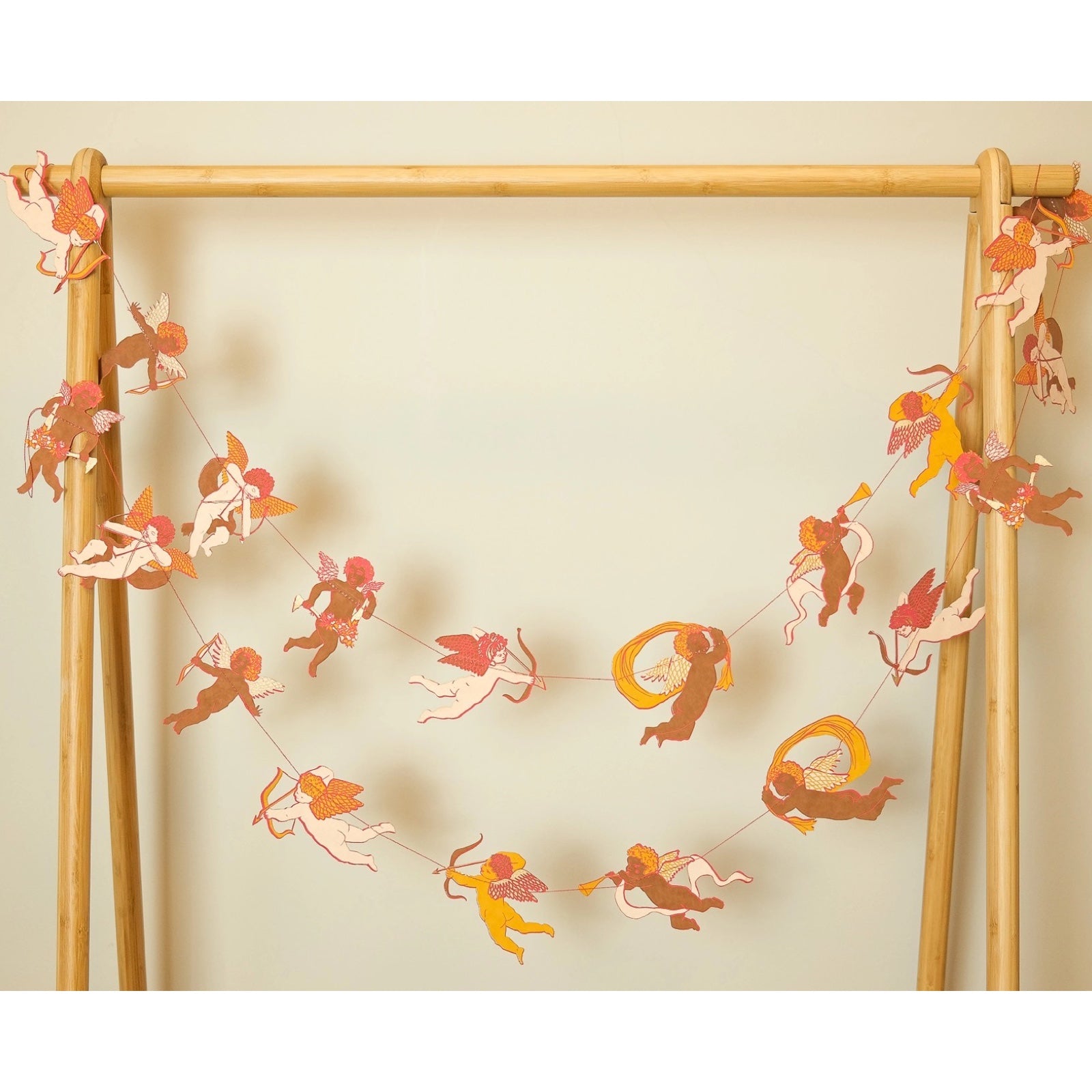 Cupid paper garland, featuring twenty screen-printed cupids ready to shoot their love arrows! Hanging from a wooden frame.