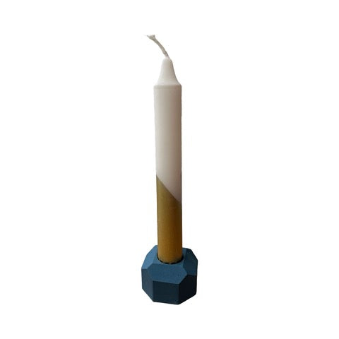 A cylindrical dinner candle holder with a lip around the bottom to catch any drips holding a blue dinner candle.