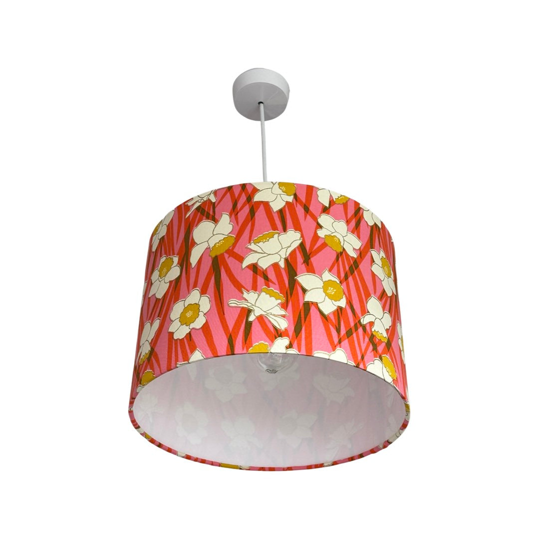 Drum lampshade covered in cotton fabric with a pink and red background and white and yellow daffodils