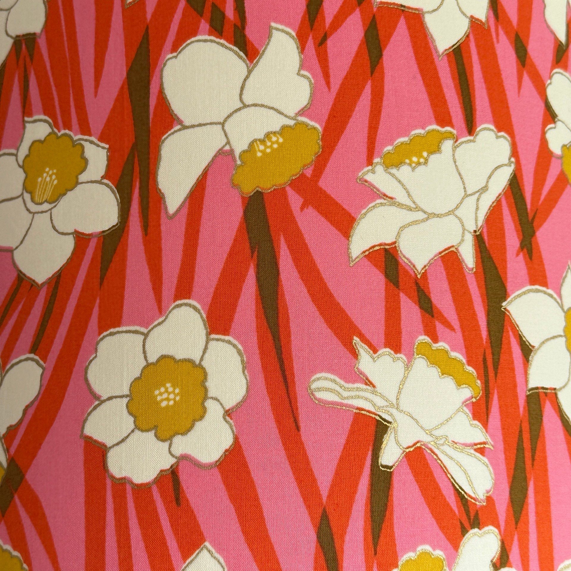 Fabric with a pink and red background and white and yellow daffodils