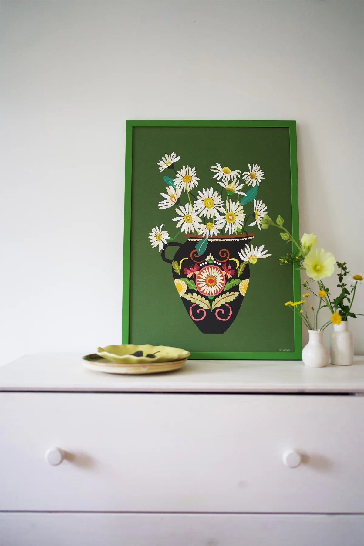 Framed artwork with floral design on a white chest of draws.