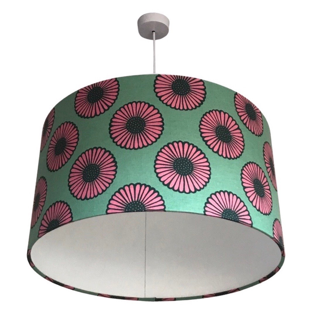 Drum lampshade covered in aqua canvas fabric with pink and black daisies and a white inner lining.