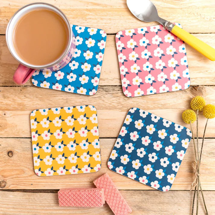 Set of four floral coasters on a wooden surface with a mug of tea.