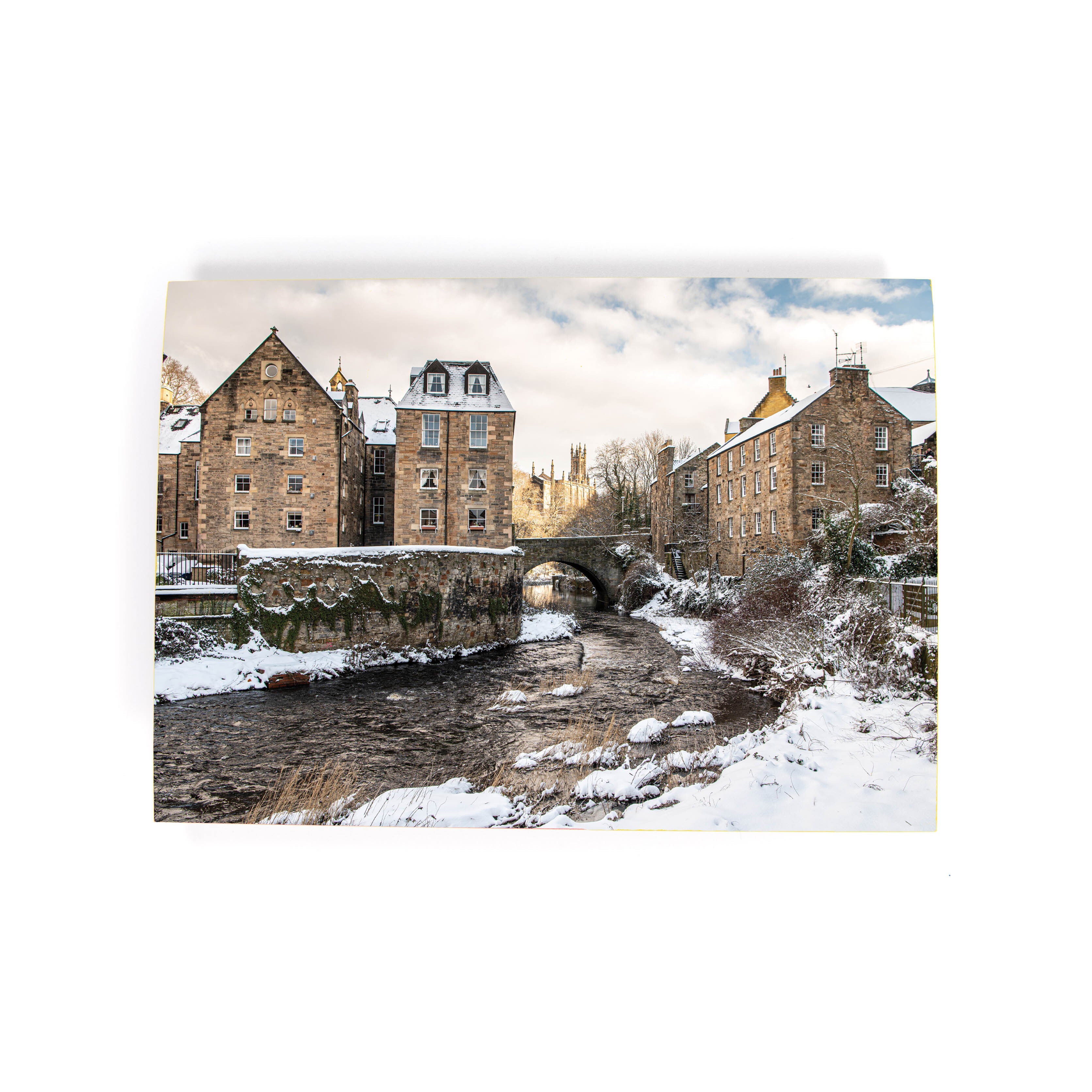A Christmas card featuring a scenic view of the Dean Village in Edinburgh with snow on the ground and a bridge connecting the two sides of the village.