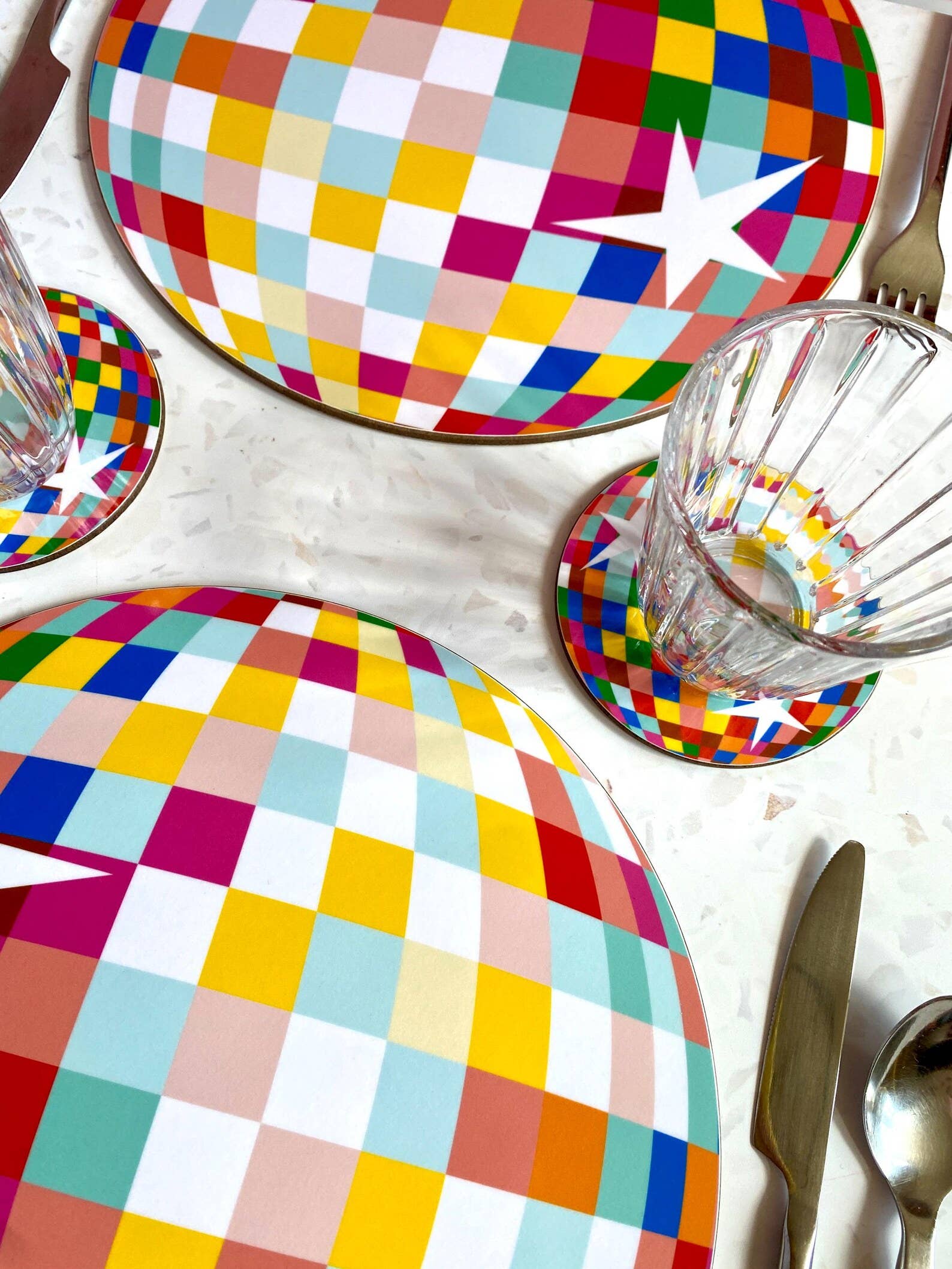 Colourful checkered disco ball and coasters on a table with cutlery and glasses.