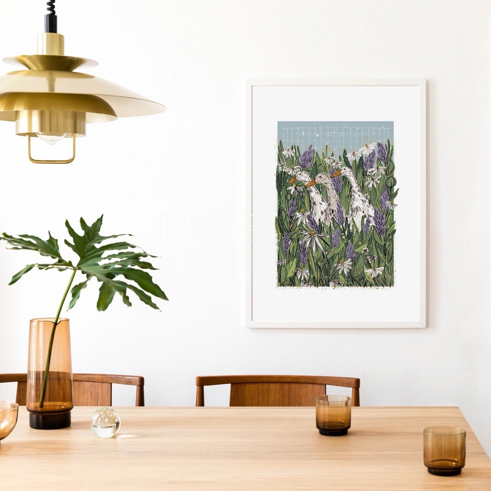 Dining room with a wooden table, chairs, a plant in a vase, and a framed artwork of ducks in a field with flowers on the wall.