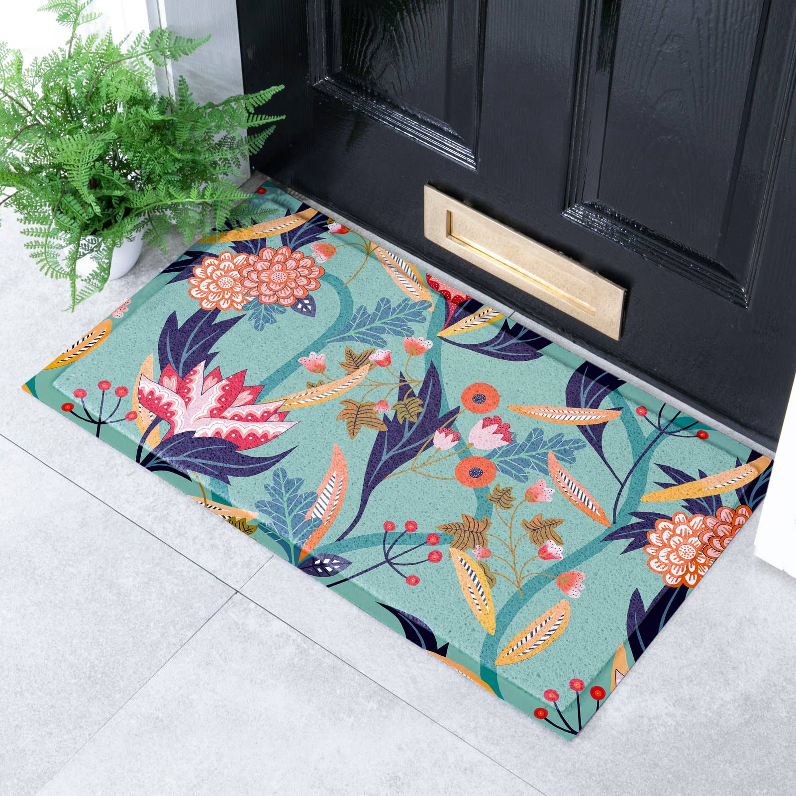A rectangular doormat with a colourful botanical floral pattern, placed in front of a black front door on a light grey tiled floor next to a potted green plant.
