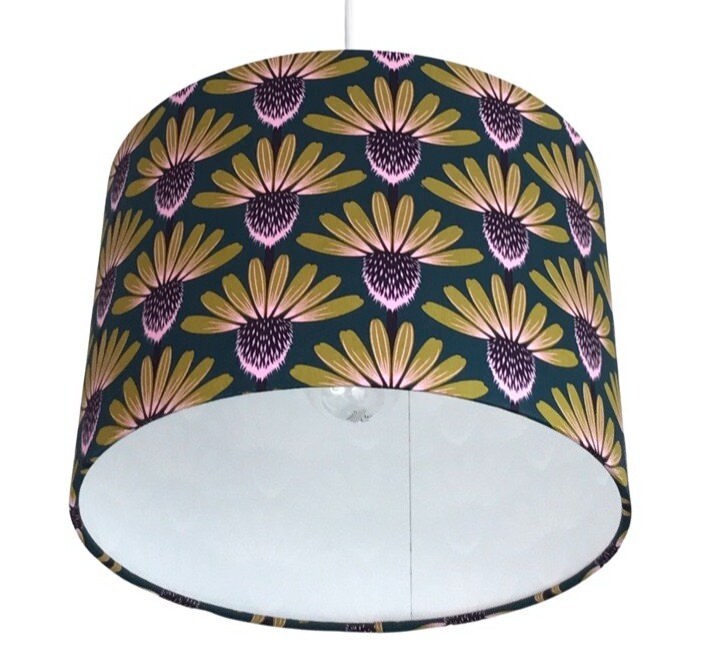 Close up of a drum lampshade with mustard and purple echinacea flowers on a navy background.