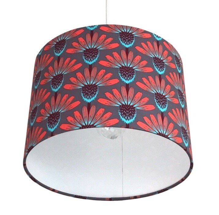 Close up of a drum lampshade covered in grey fabric with red, brown and blue echinacea flowers