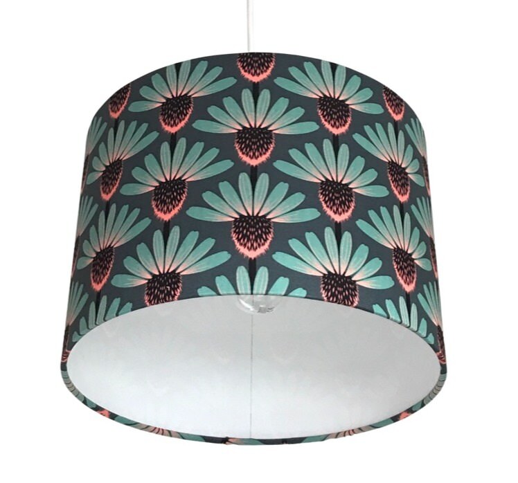 Close up of a drum lampshade with teal, brown and pink echinacea flowers on a teal background.