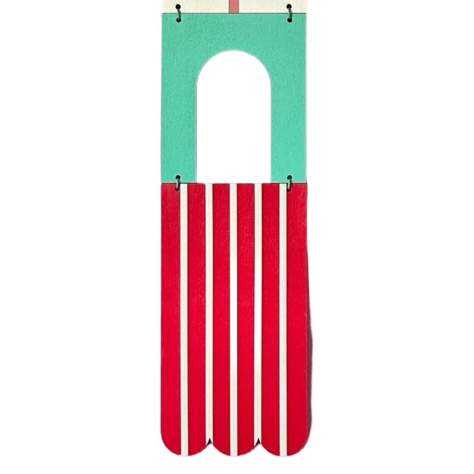 A geometric modern wall art hanging in red, green, black, and white with a waxed cord and wooden beads.