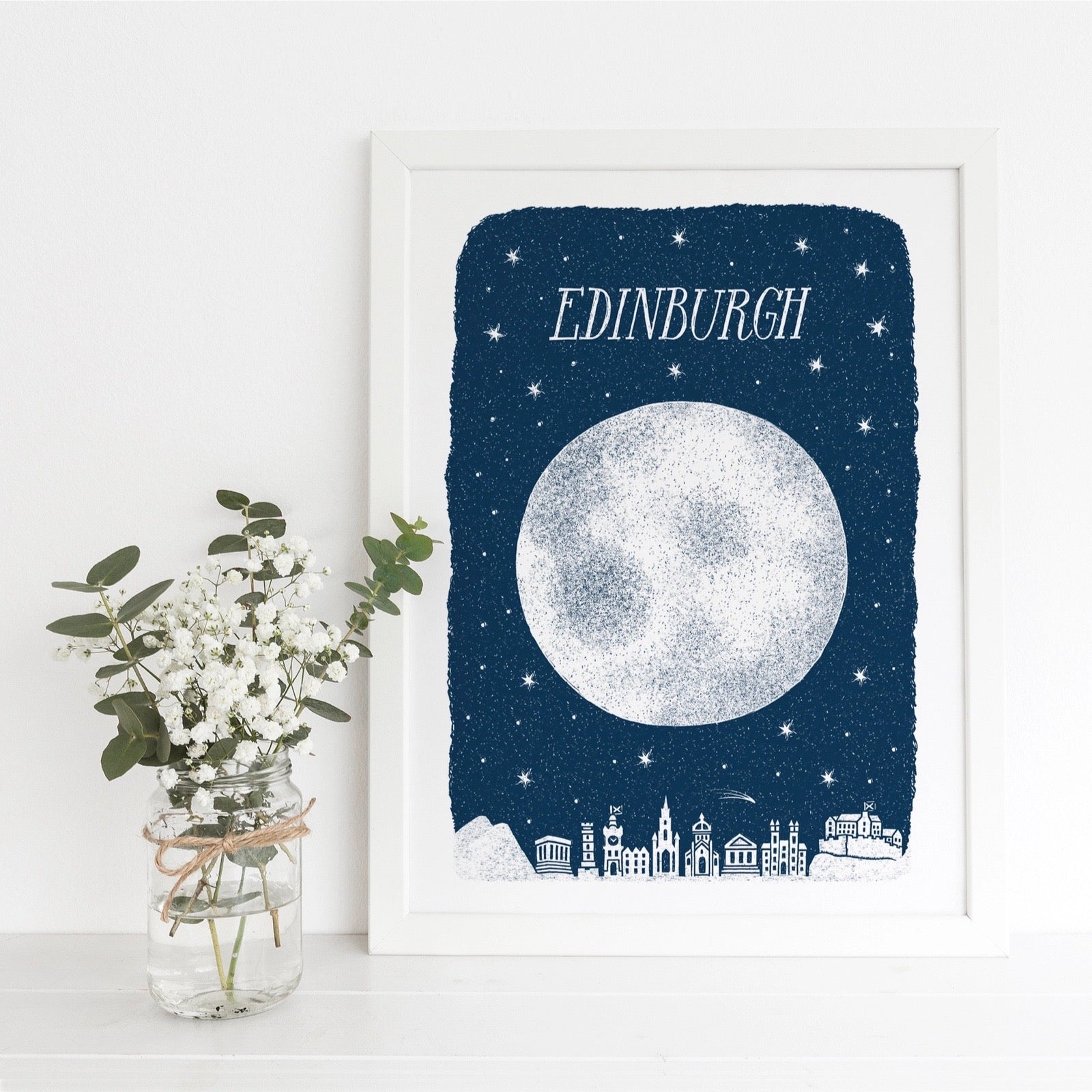 Framed artwork with moon and cityscape on a blue background, featuring the word 'Edinburgh'.