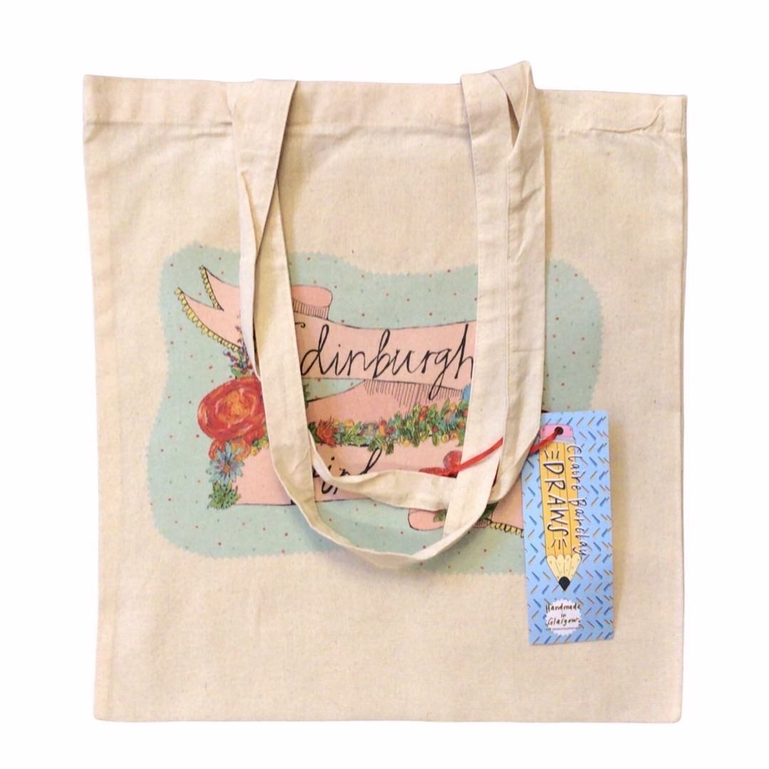 Tote bag featuring the text 'Edinburgh Girl' written inside a banner and surrounded by flowers on a blue spotty background.