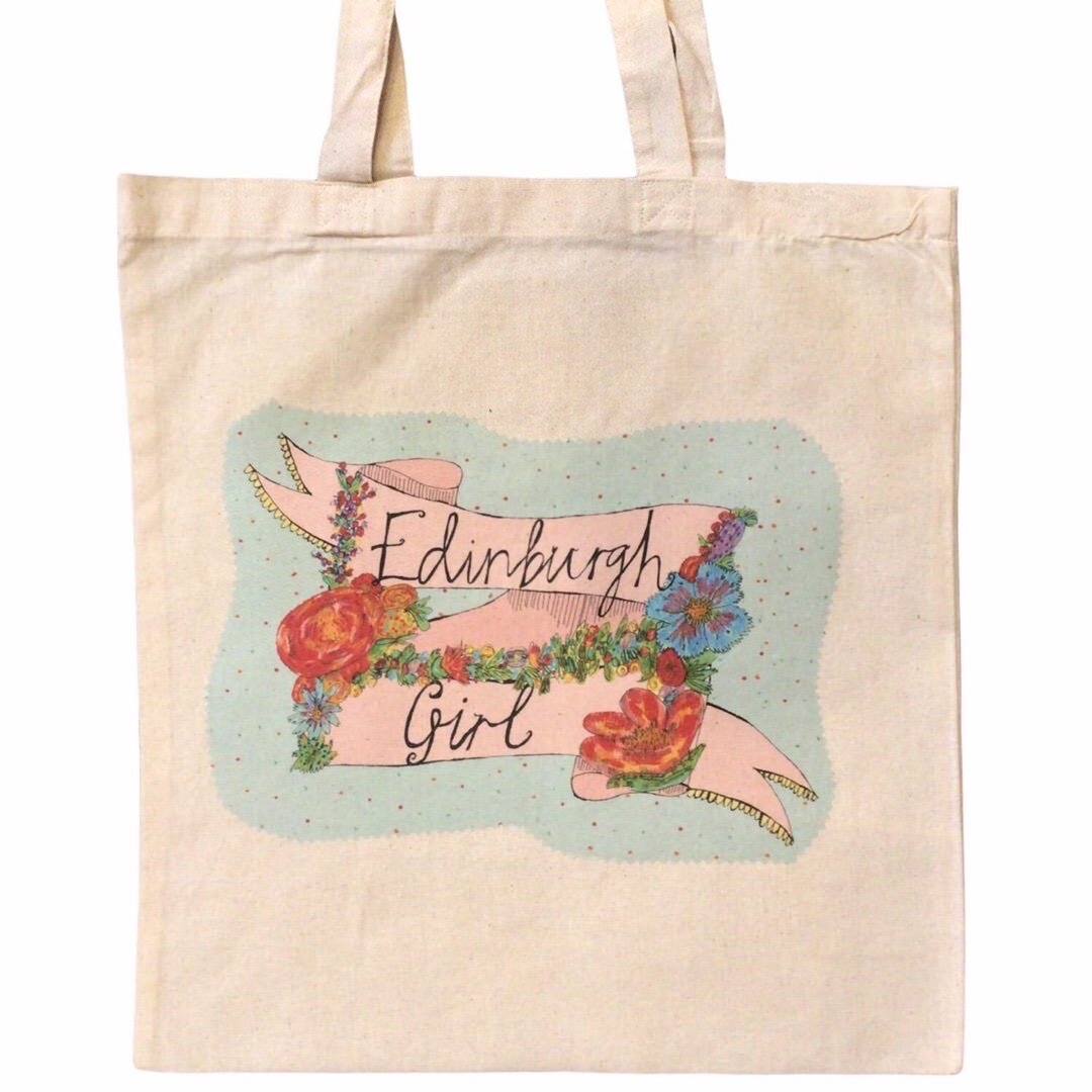 Tote bag featuring the text 'Edinburgh Girl' written inside a banner and surrounded by flowers on a blue spotty background.