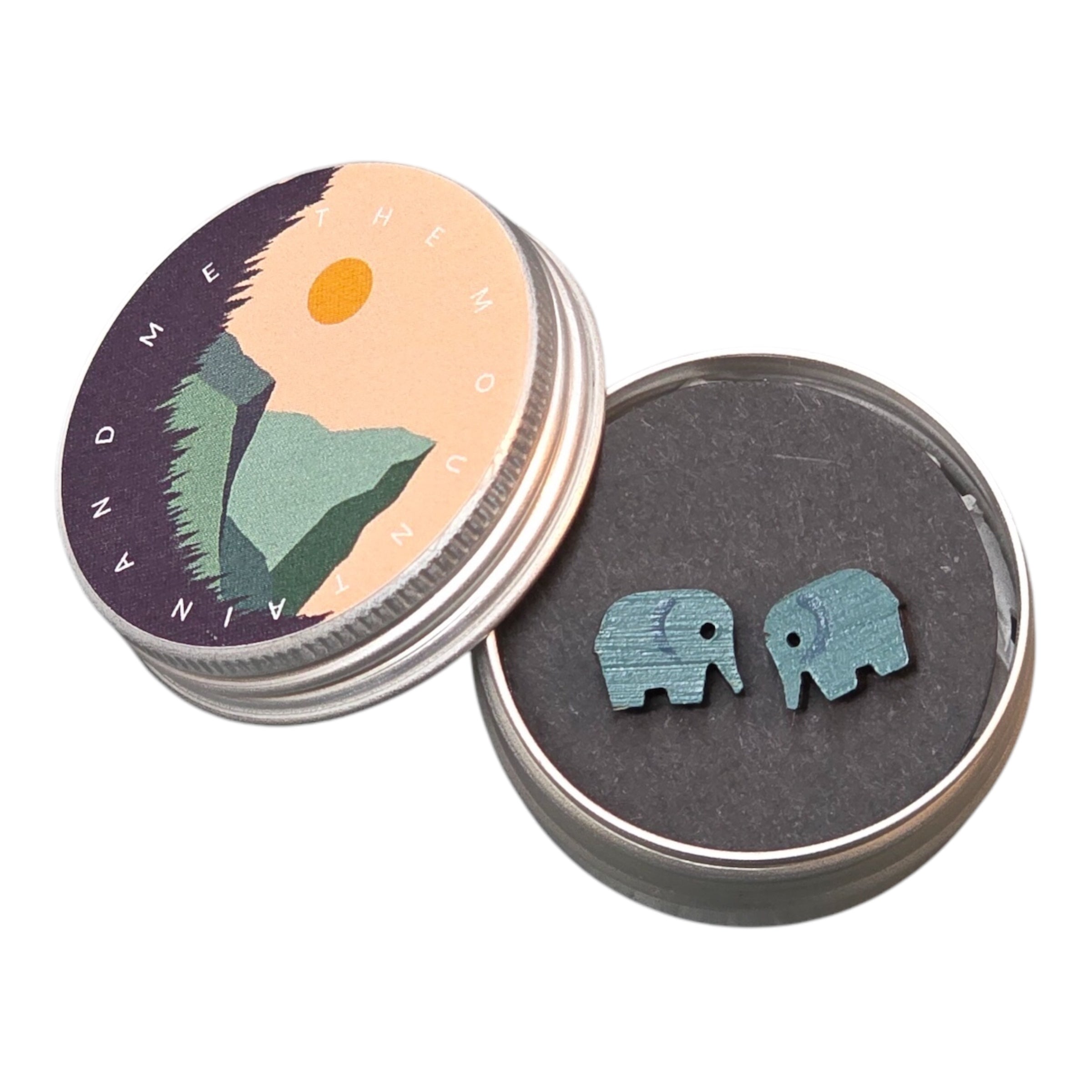 A pair of grey elephant-shaped wooden earrings in a small tin.