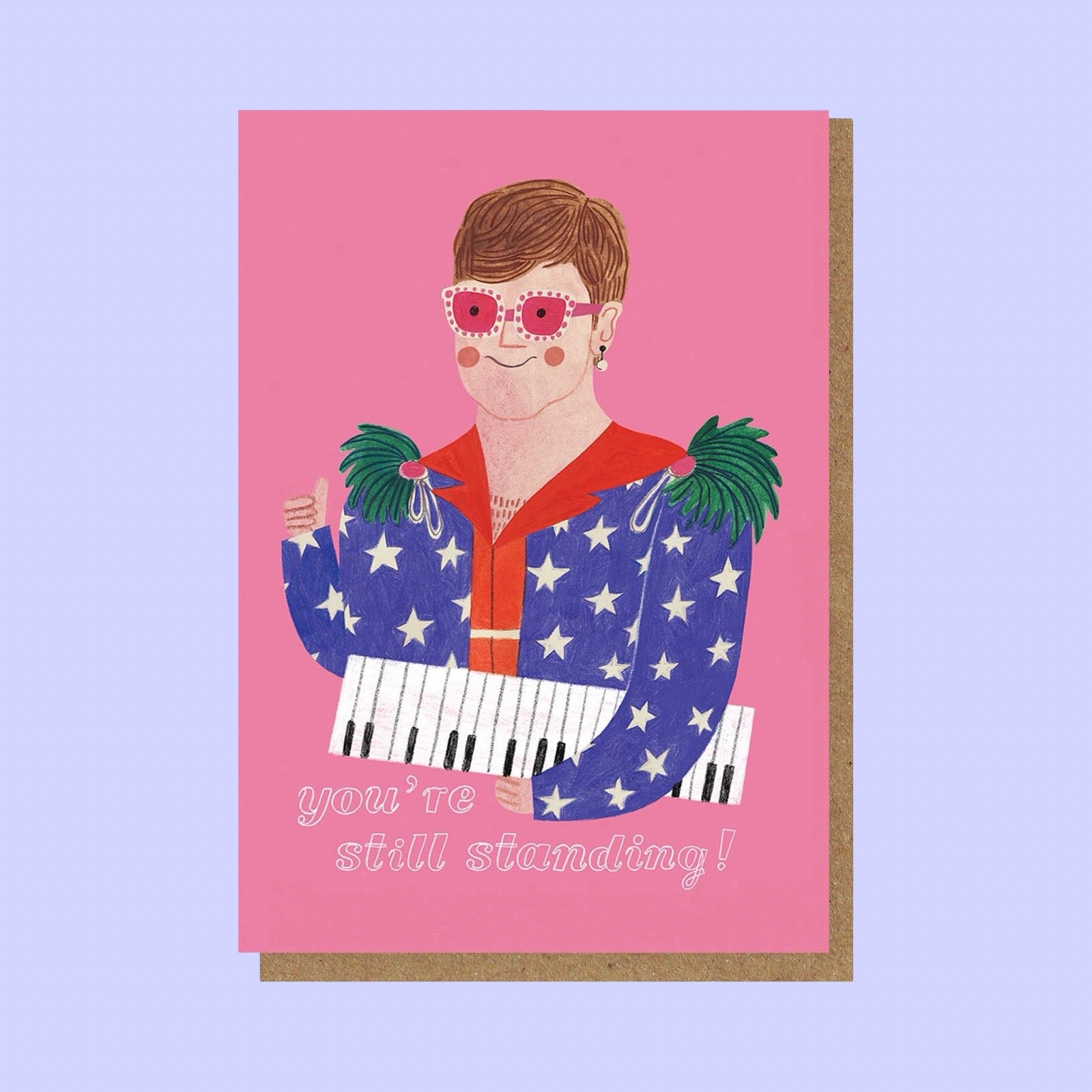 Card with illustration of Elton John wearing sunglasses and a colourful outfit, with text 'you're still standing!', on a pink background on a brown envelope, with a lilac background.
