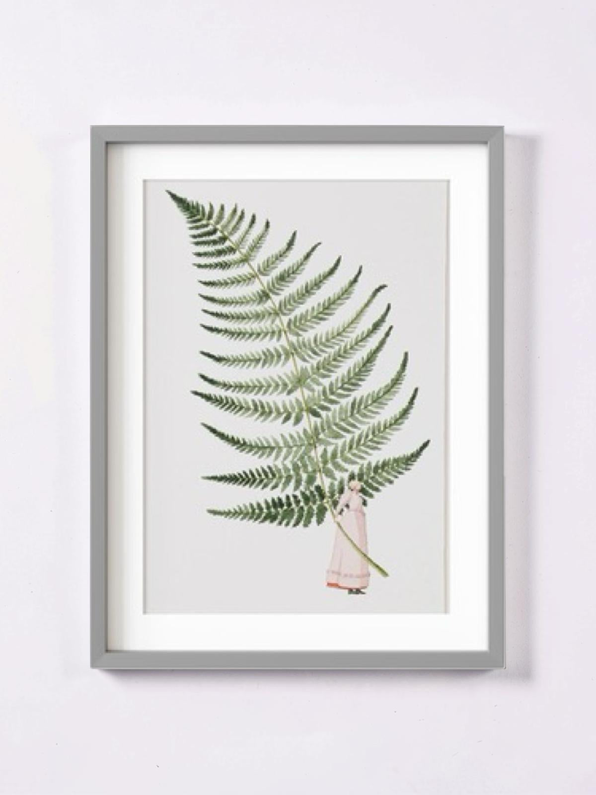 A print of a giant fern leaf being held by a lady dressed in a long flowing pale pink dress.