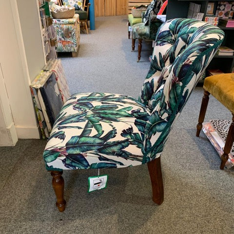A button-back chair with off-white velvet fabric featuring a blue and green fern design, cream binding, mahogany legs, and gold castors.