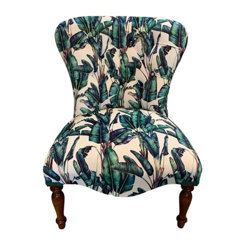 A button-back chair with off-white velvet fabric featuring a blue and green fern design, cream binding, mahogany legs, and gold castors.