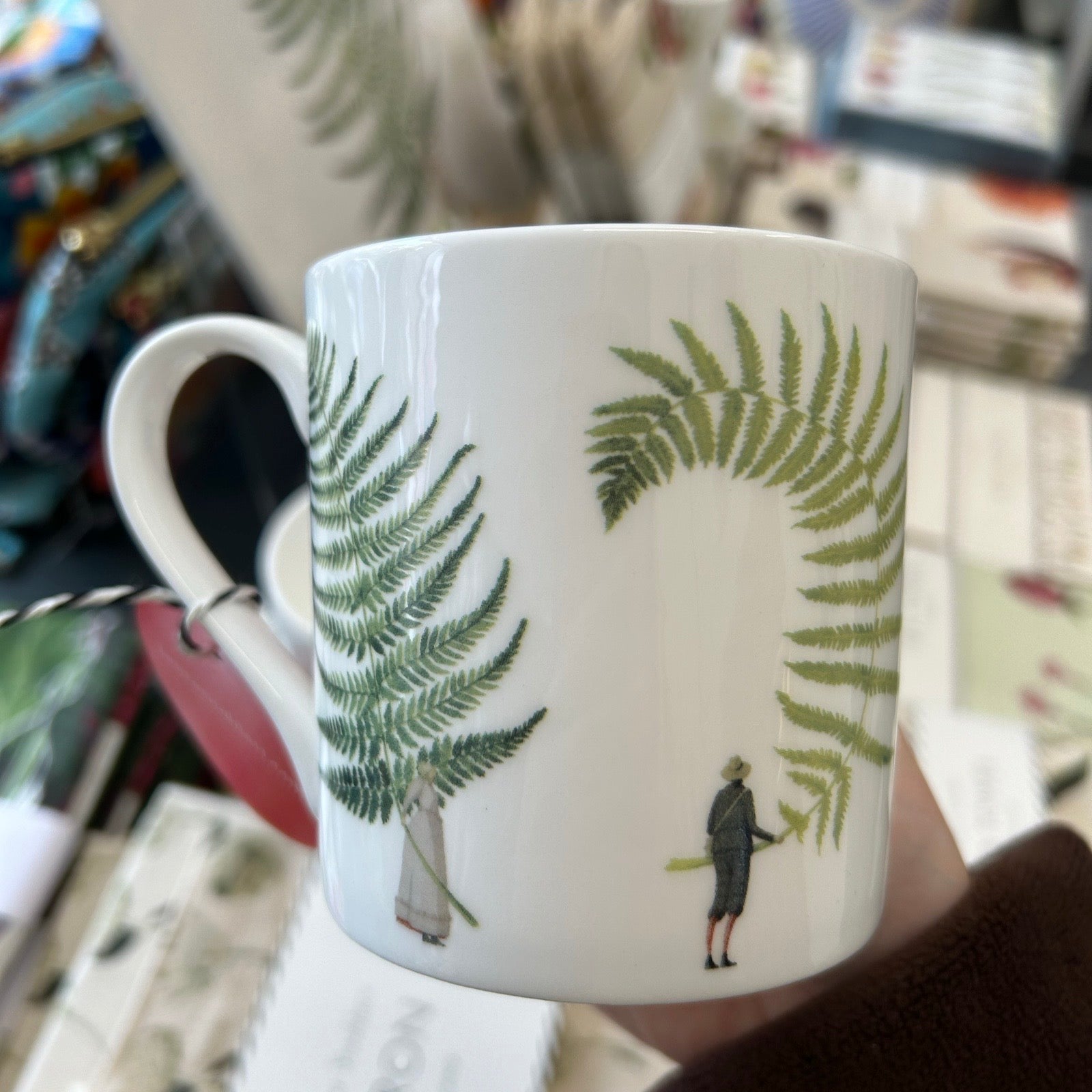 White mug with green leaf patterns held in a hand against a blurred background.