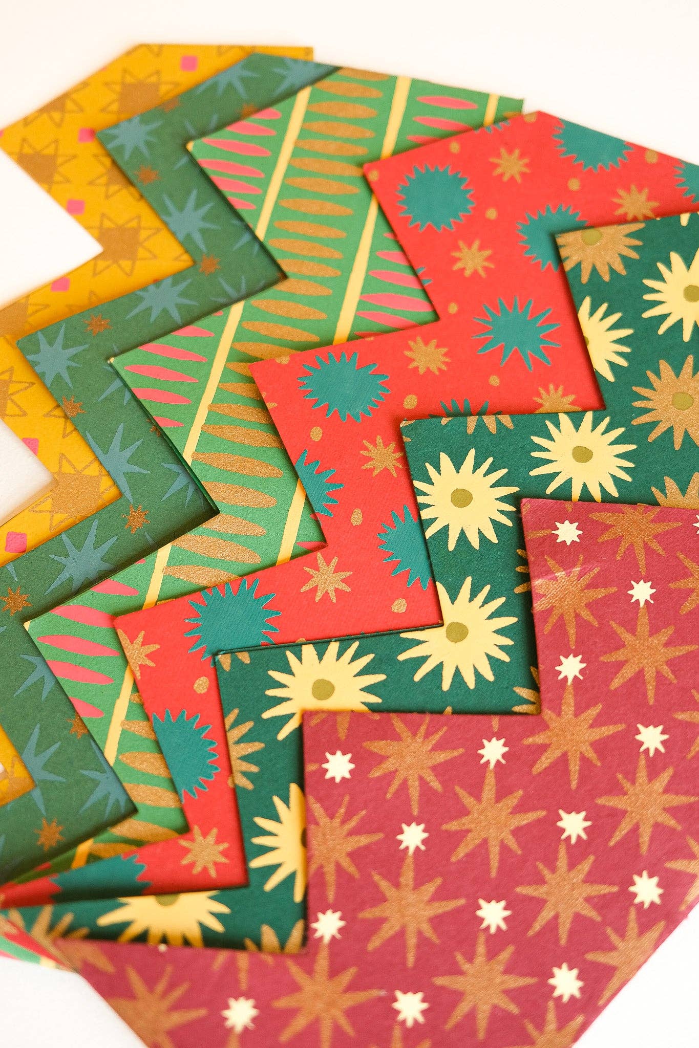 A fan arrangement of colourful patterned crowns in red, green, yellow, and pink, each with starburst, stripe, and floral motifs on a white background.