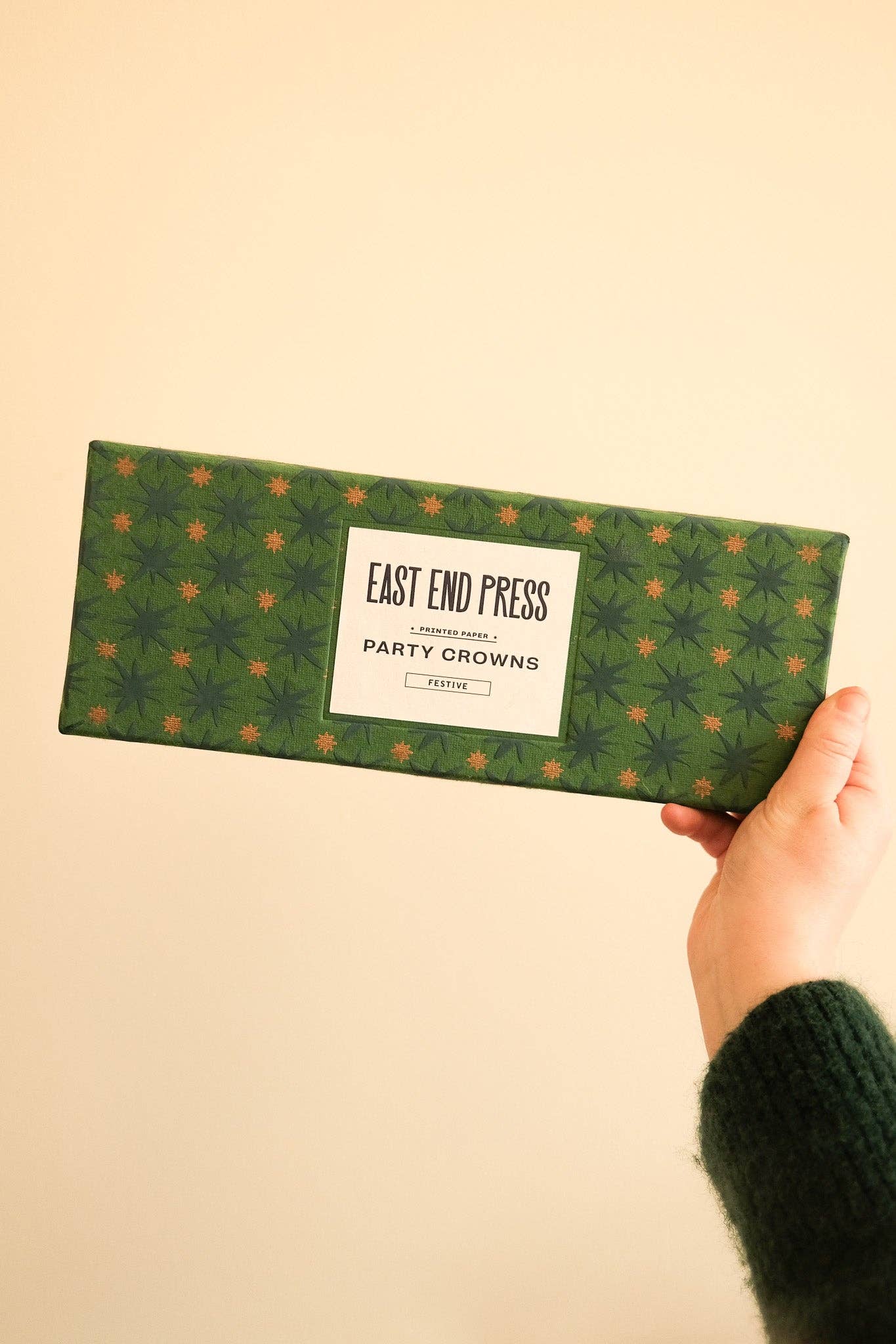 Hand holding a green box with 'East End Press' branding on a beige background.