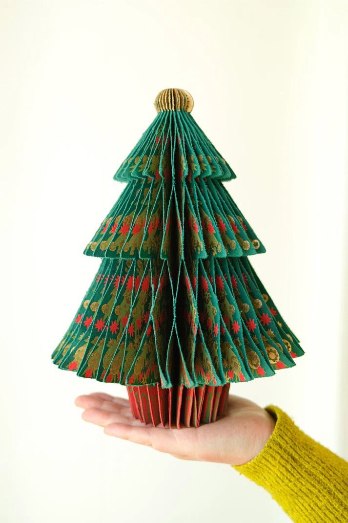 Hand holding a folded paper Christmas tree with green, red, and gold colours on a white background.