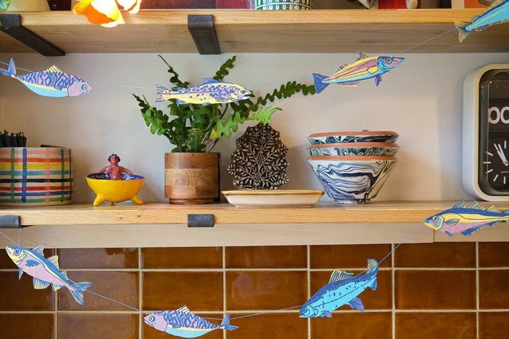Decorative shelf with plants, bowls, and a clock against a tiled wall.