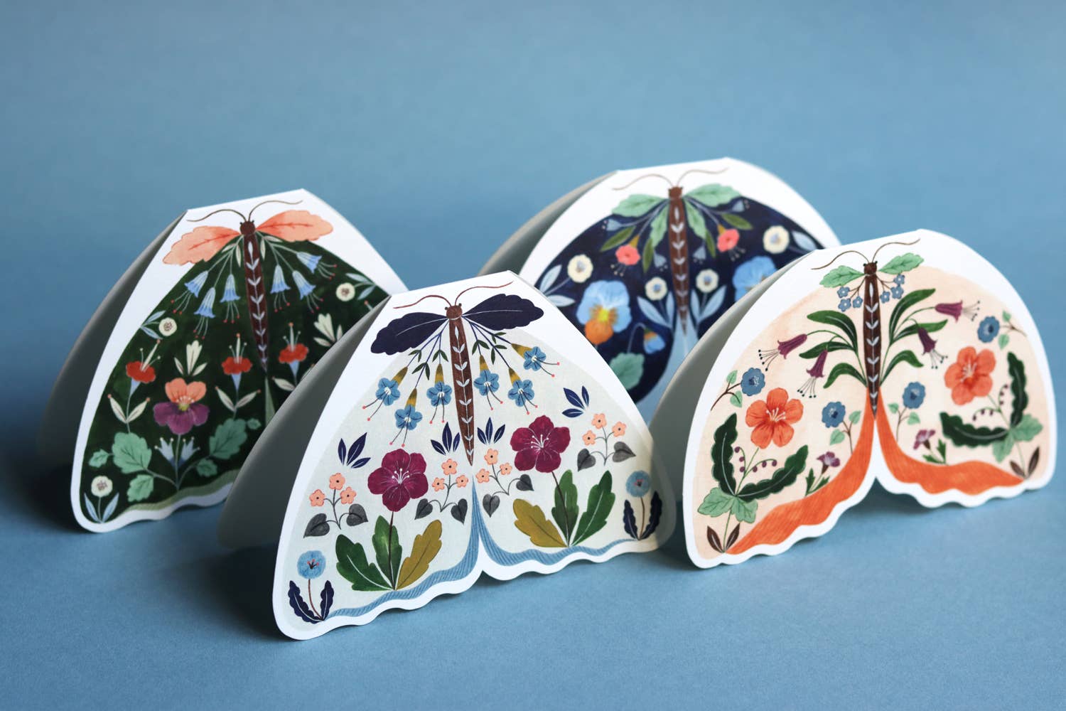 Four decorative moth cards with floral patterns on a blue background.
