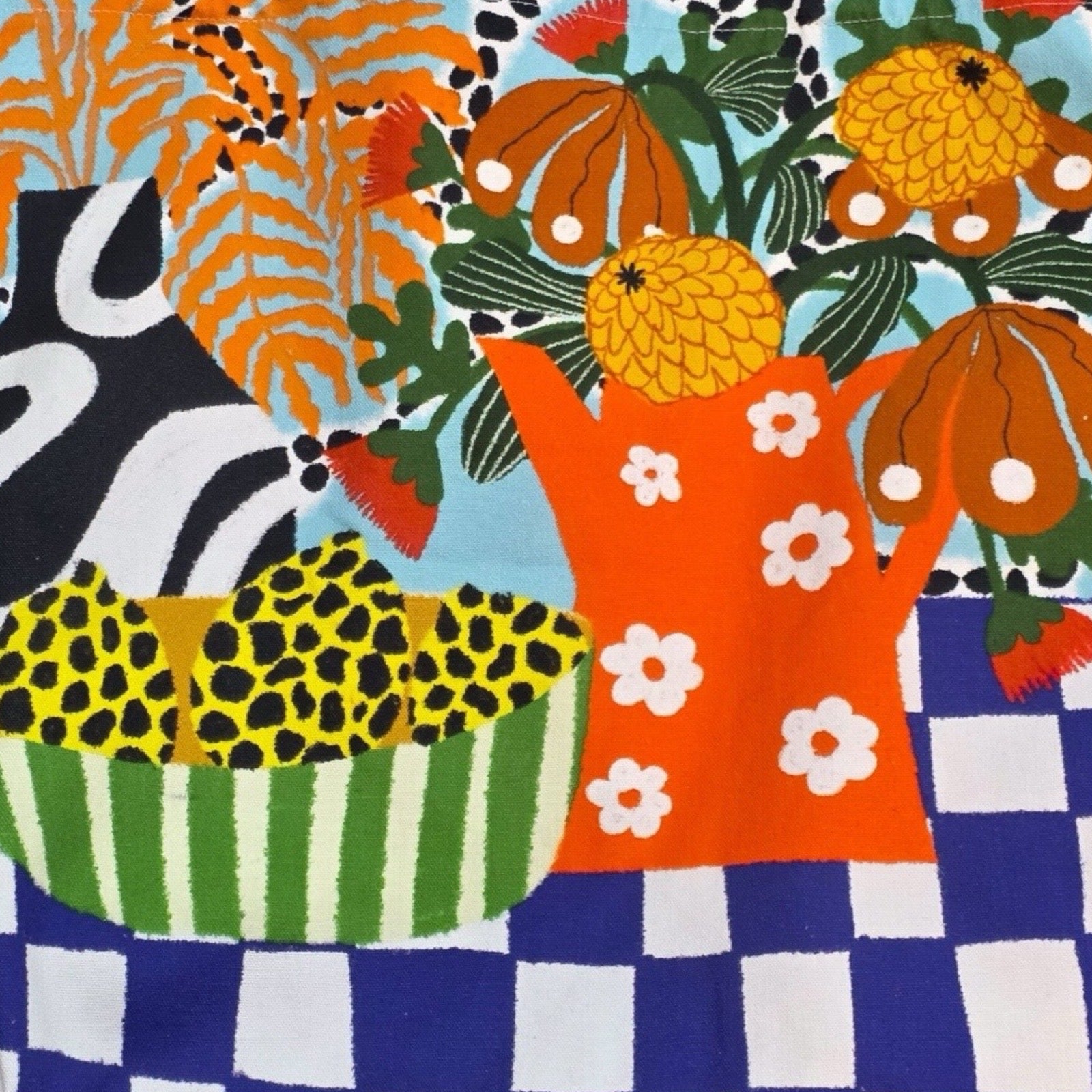 A bright and colourful tote bag featuring a black and white vase with orange leaves, a red jug with white daisies full of colourful flowers and a blue and white checked base.