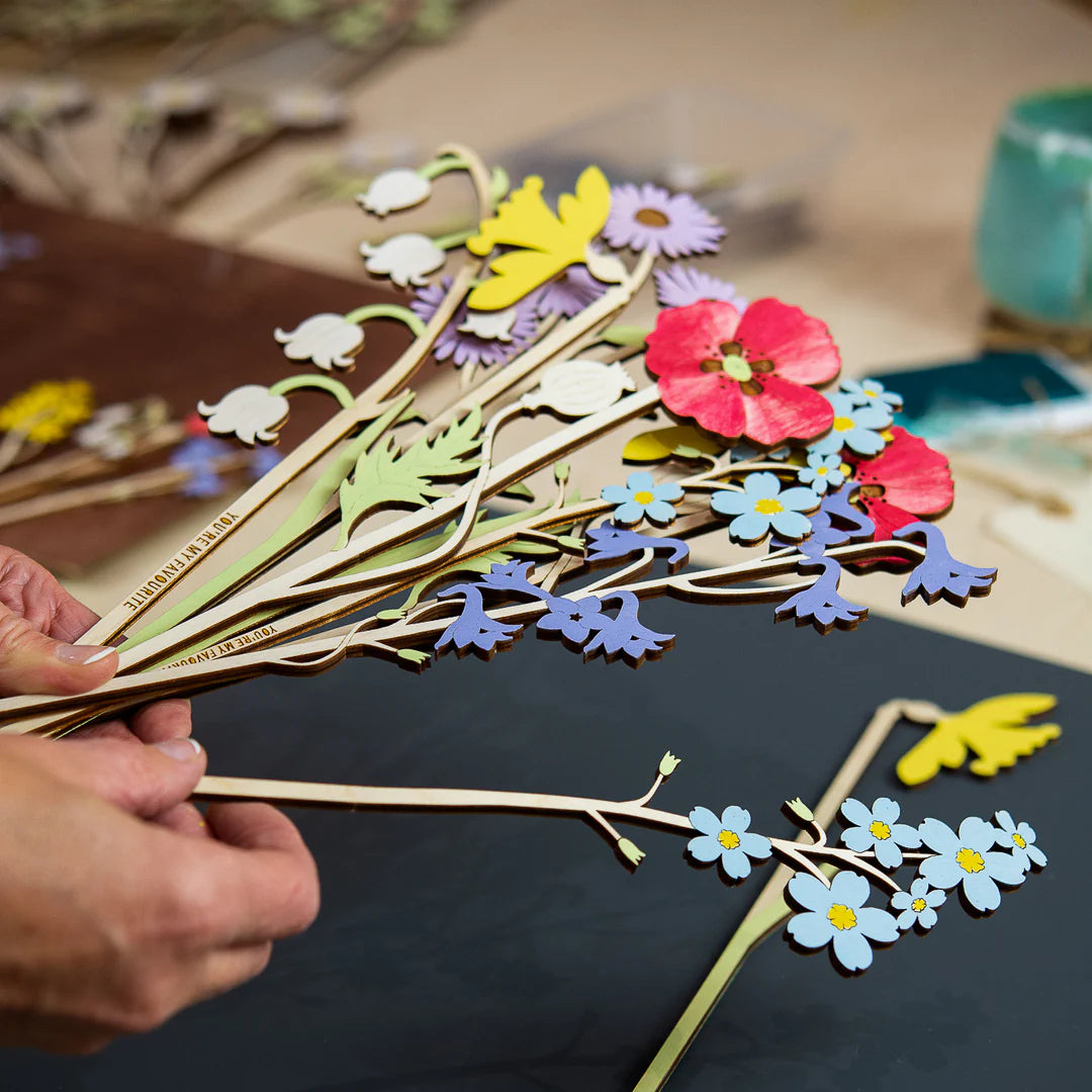 Hands holding a stack of single stem wooden flowers in a art studio.