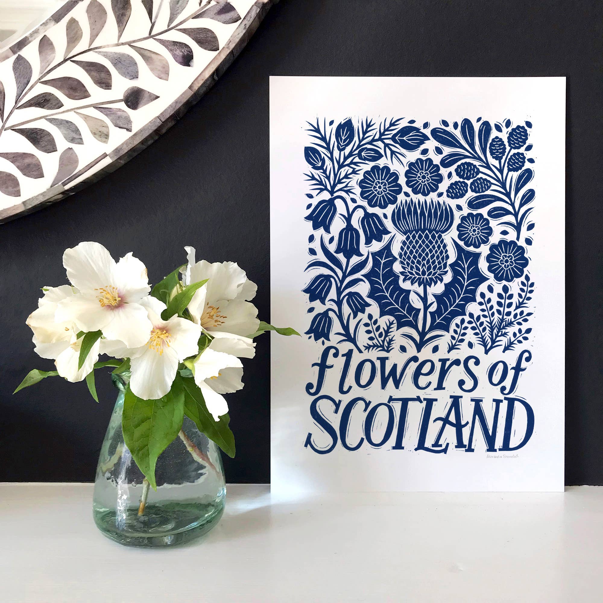 Decorative print with floral design and 'Flowers of Scotland' text next to a vase with white flowers.