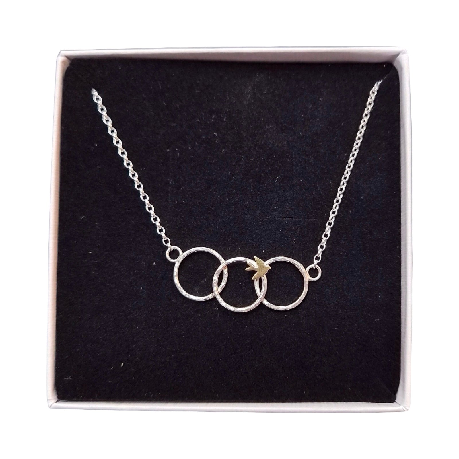 Silver necklace with interlocking rings and a bird on a black cushion in a box.