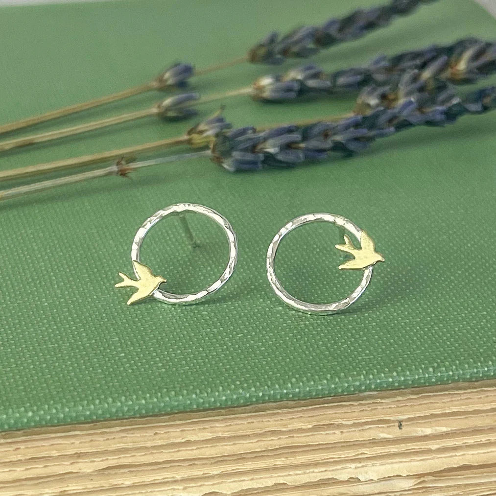 Silver hoop earrings with bird designs on a green surface with lavender.