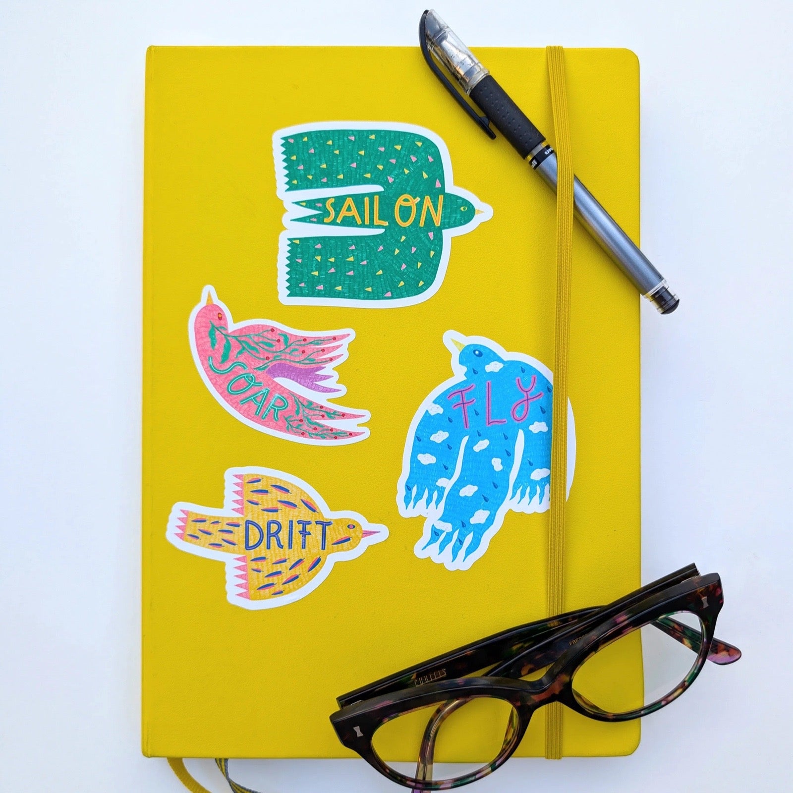 Yellow notebook with colourful stickers and a pen on a white background.