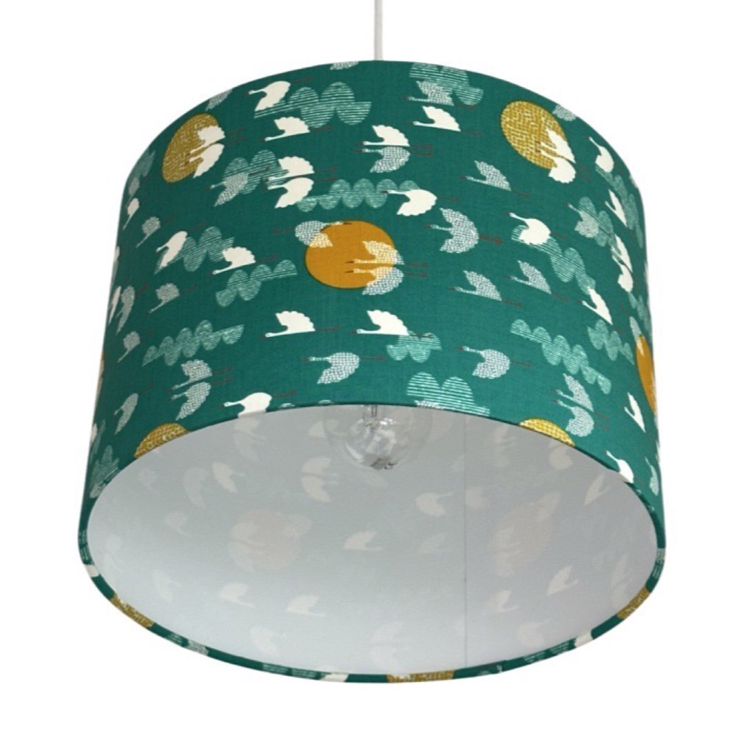 Close up of a drum lampshade covered in green cotton fabric with white flying birds and mustard moons.