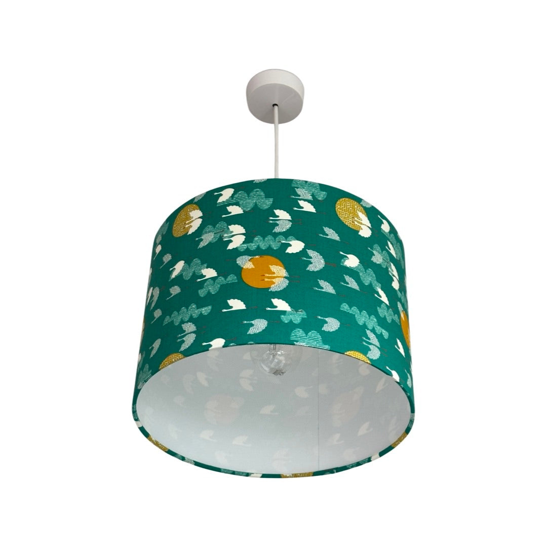 Drum lampshade covered in green cotton fabric with white flying birds and mustard moons.