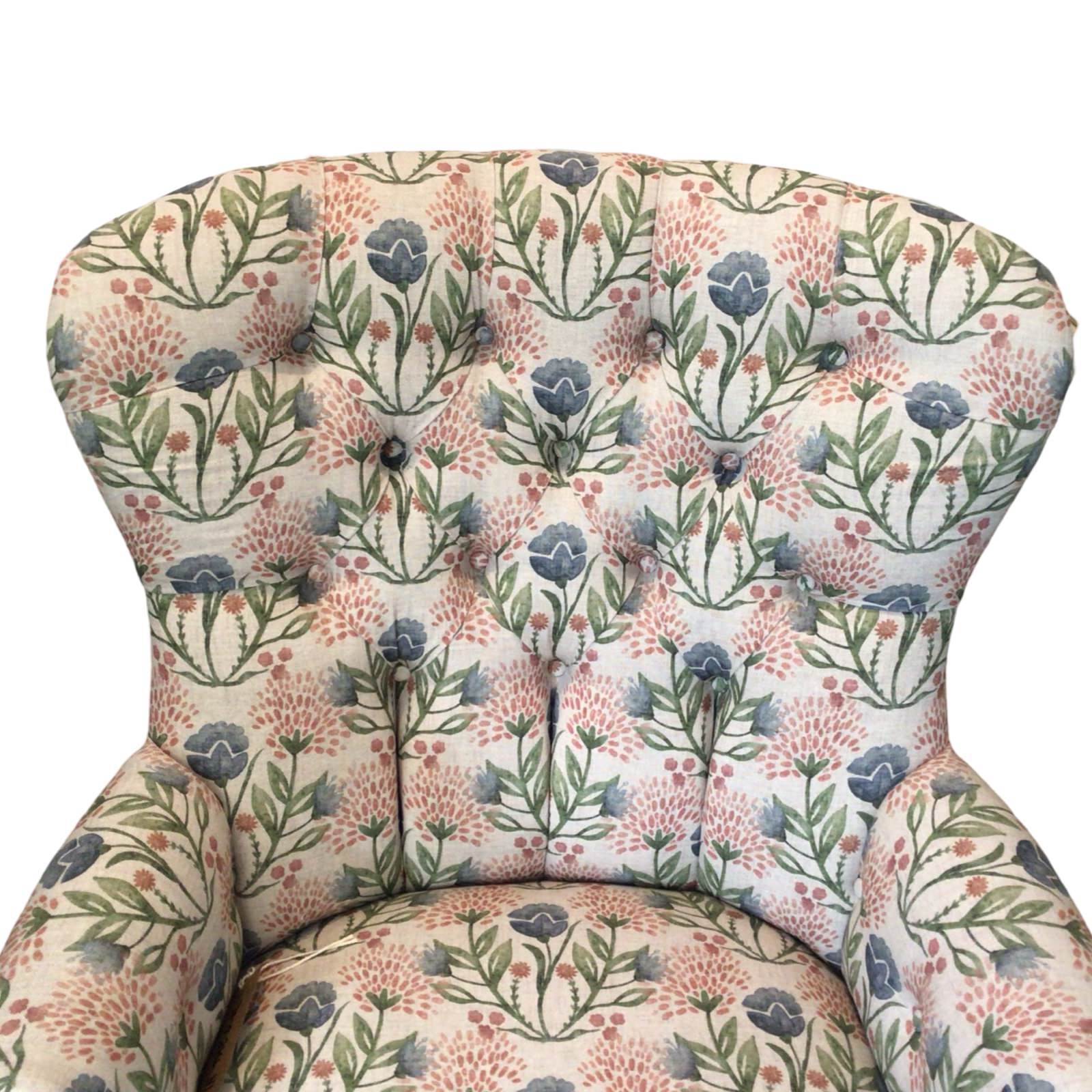 A cream linen armchair with pink and pale blue floral pattern, featuring mahogany legs and gold castors, upholstered with a button-back design.