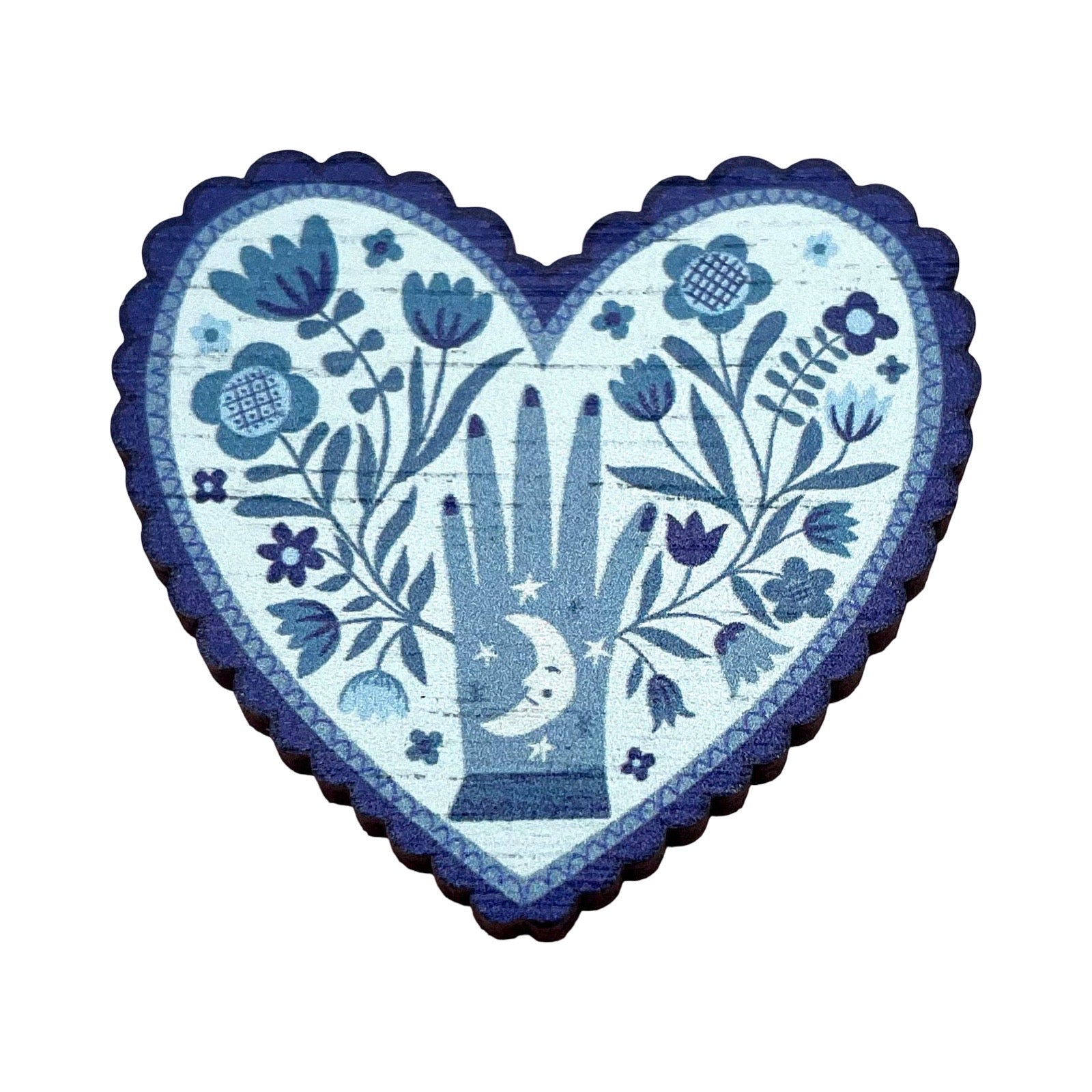 A heart-shaped decorative brooch featuring a hand-painted folk art design in shades of blue and white, with a central praying hand, flowers, and a crescent moon, shown on a plain white background.