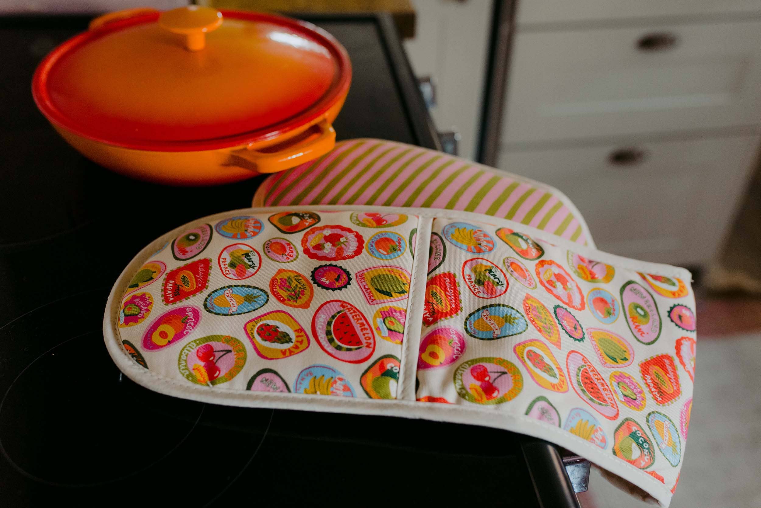 Colorful oven mitt with fruit pattern on a stove.