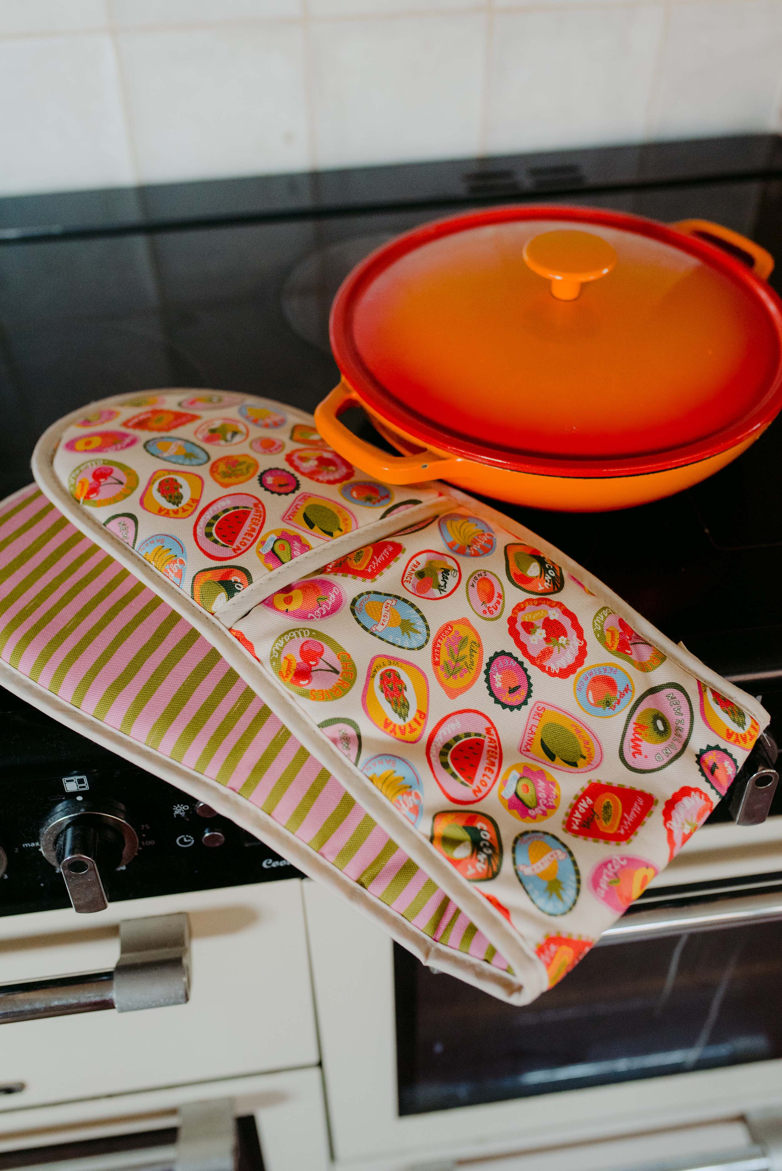 Colourful pot holder and trivet on a stove with an orange lid.