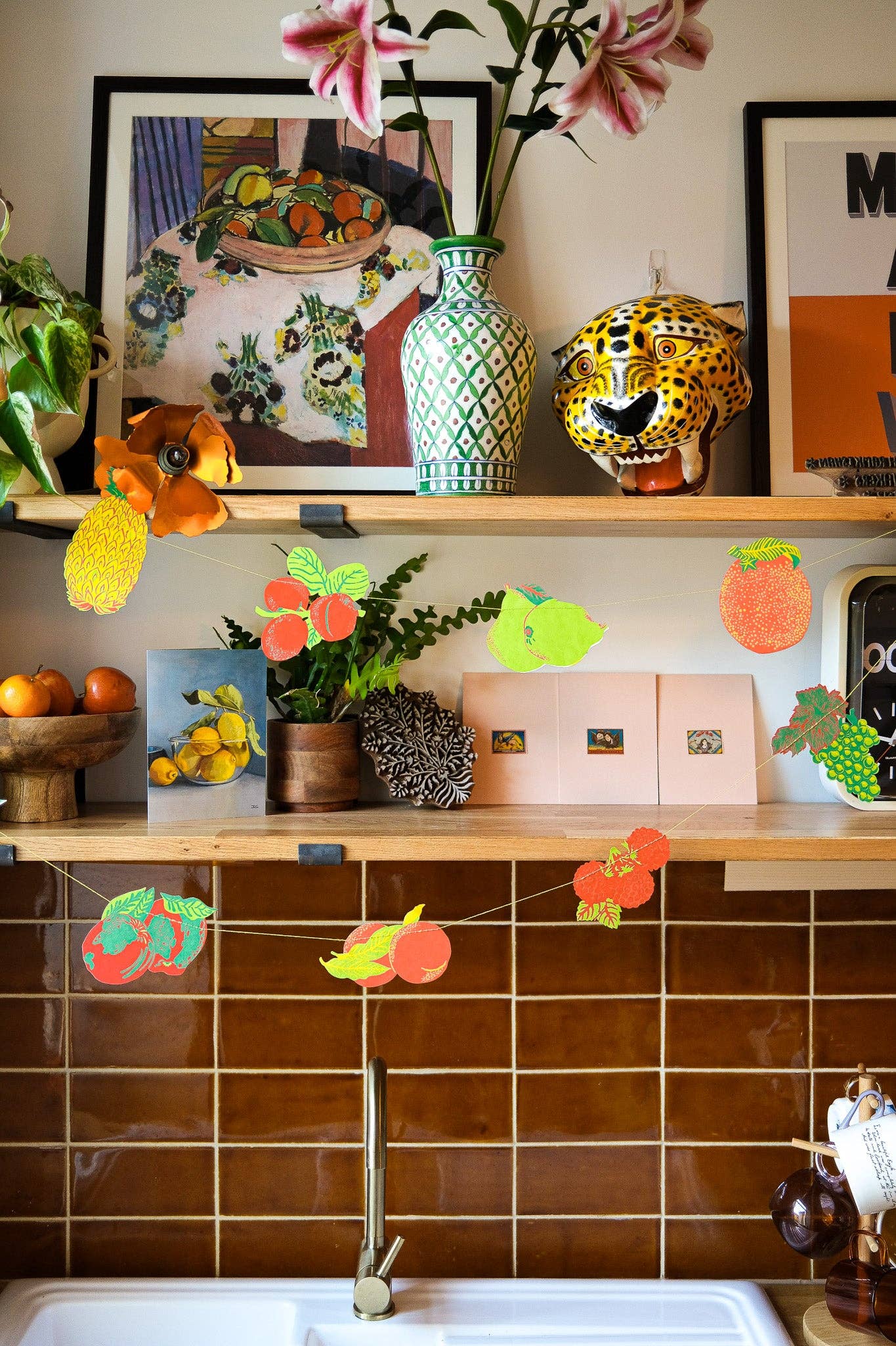 Decorative kitchen shelf with plants, vases, and colorful paper decorations against a tiled wall.