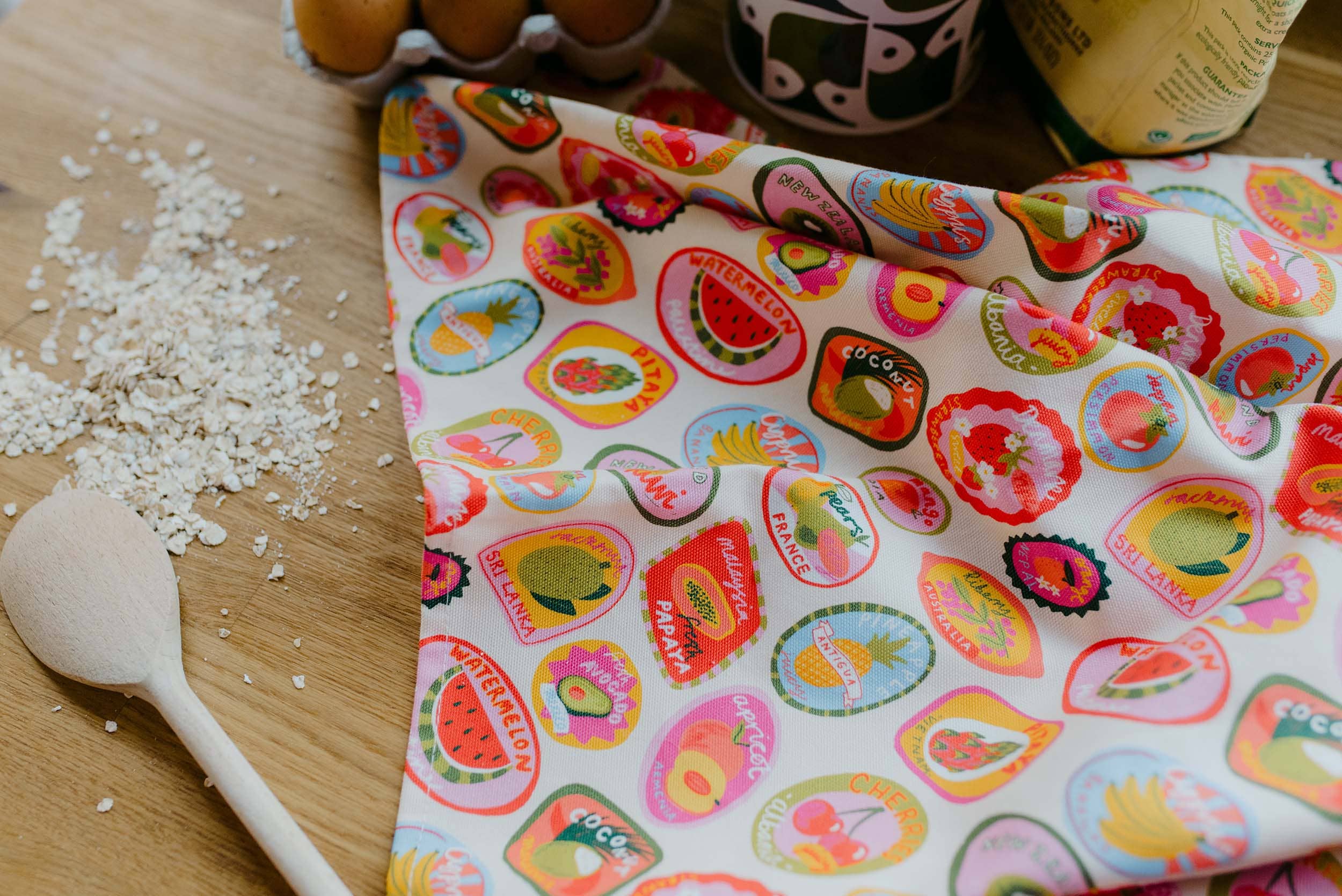 Colourful fabric with fruit patterns on a wooden surface with oats and a spoon.