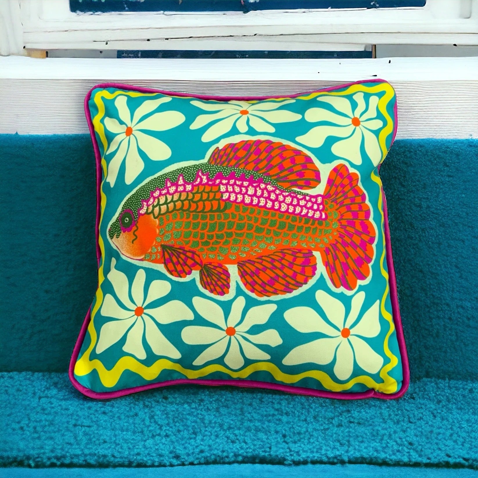 Colourful cushion with a fish design on a blue couch.